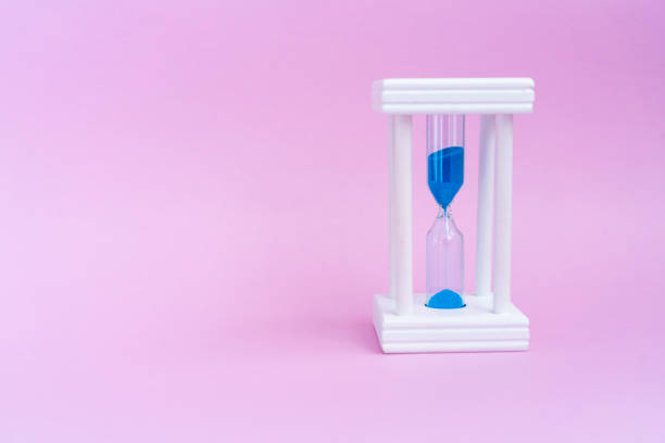 istock Elegant hourglass with running blue sand on pink background with copy space 1155385478