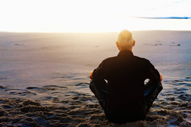 Motorcyclist sitting cross-legged, meditating, on beach at sunset