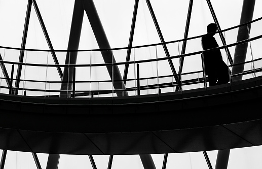 Desaturated image depicting the back lit silhouette of a city worker walking down a winding spiral staircase inside his office building. The image is full of leading lines and interesting geometric shapes which are further accentuated by the black and white look of the photo.