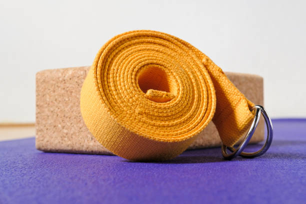 accesorios para practicar yoga. ladrillo de corcho y correa amarilla en alfombra morada. - purple belt fotografías e imágenes de stock
