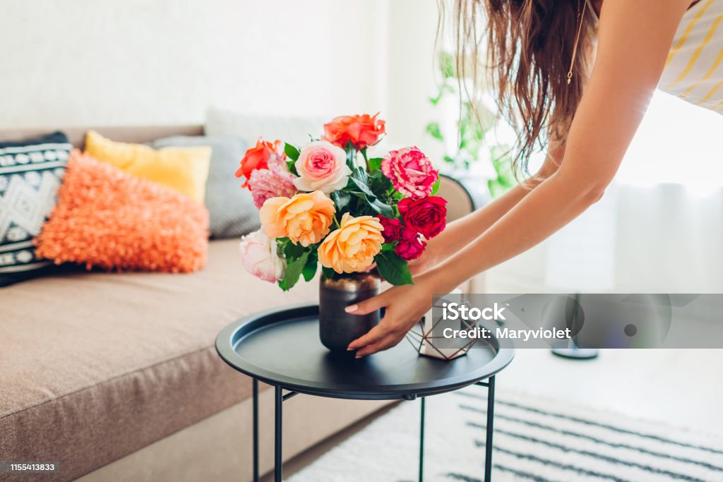 Woman puts vase with flowers roses on table. Housewife taking care of coziness in apartment. Interior and decor Woman puts vase with flowers roses on table. Housewife taking care of coziness in apartment. Interior design and decor Flower Stock Photo