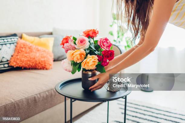 Woman Puts Vase With Flowers Roses On Table Housewife Taking Care Of Coziness In Apartment Interior And Decor Stock Photo - Download Image Now