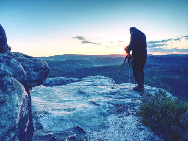 istock Photographer with tripod on cliff and thinking. Dreamy landscape 1155417289