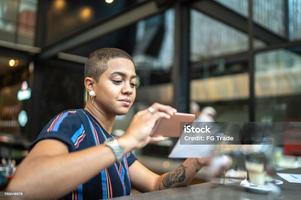 Young woman depositing check by phone in the cafe Banking Stock Photo