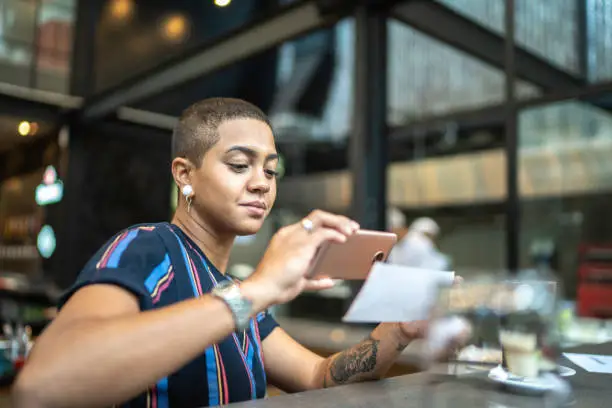 Photo of Young woman depositing check by phone in the cafe