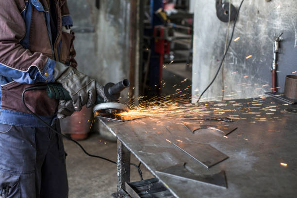 istock Workman with a mask and gloves is grinding a metal object with a grinder. He wears a protective wardrobe. 1155420481