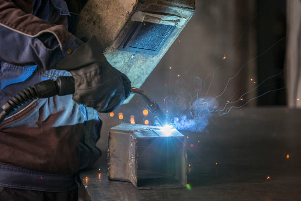 istock Worker in a protective wardrobe with a mask and gloves is welding a metal objects in a metal workshop. 1155420941