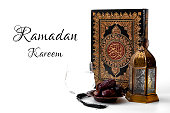 Ramadan Kareem, Muslim religious tradition, holy month of Islam and Iftar concept theme with a bowl of dates, prayer beads, glass of water, Quran and Arabic lantern on white background