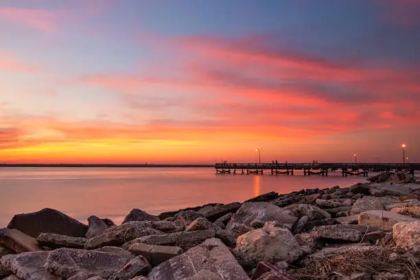 Photo of Vibrant pink and orange sunset over a fishing pier and rock jetty.