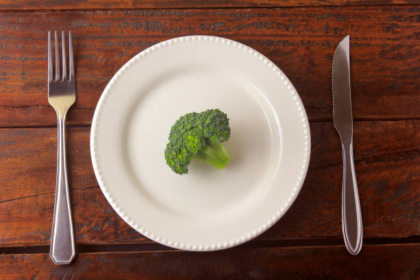 istock Concept of calorie restriction. Strict diet. Sliced pod isolated on white plate with fork and knife on wooden table 1155427013