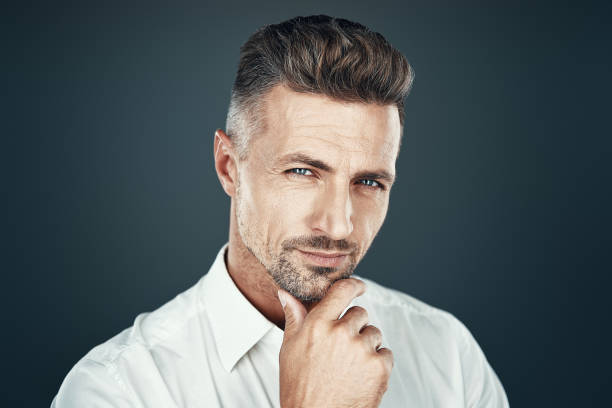 istock So charming! Handsome young man smiling and looking at camera while standing against grey background 1155427151