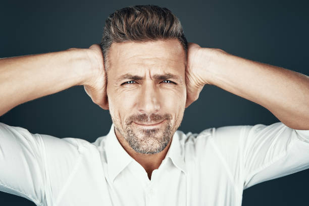 istock Oh no! Frustrated young man covering ears with hands and making a face while standing against grey background 1155427290