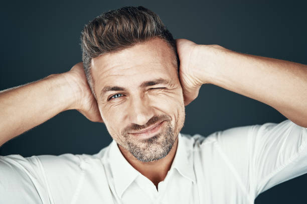 istock Winking to you. Handsome young man smiling and looking at camera while standing against grey background 1155427318