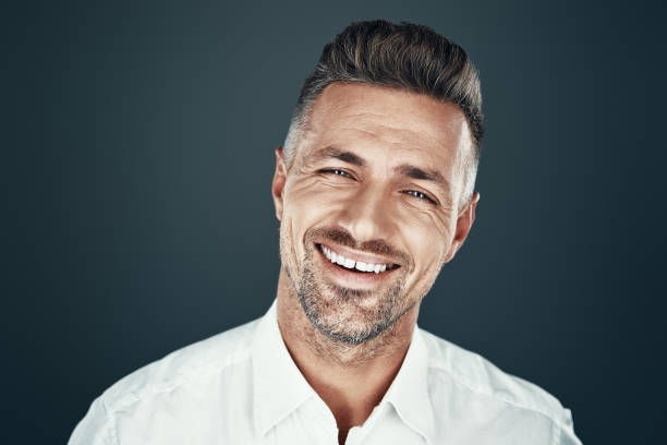 istock Positively minded. Handsome young man smiling and looking at camera while standing against grey background 1155428394