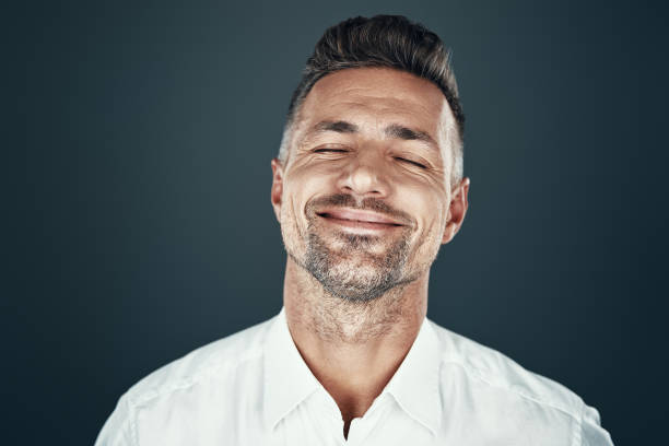 Enjoyment. Handsome young man smiling and keeping eyes closed while standing against grey background