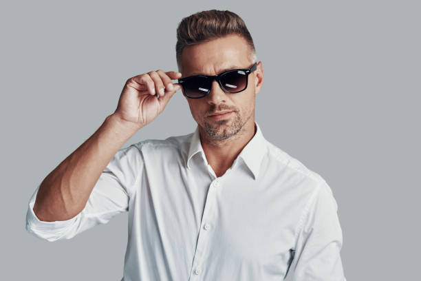 istock In his own style. Handsome young man looking at camera and adjusting sunglasses while standing against grey background 1155429077