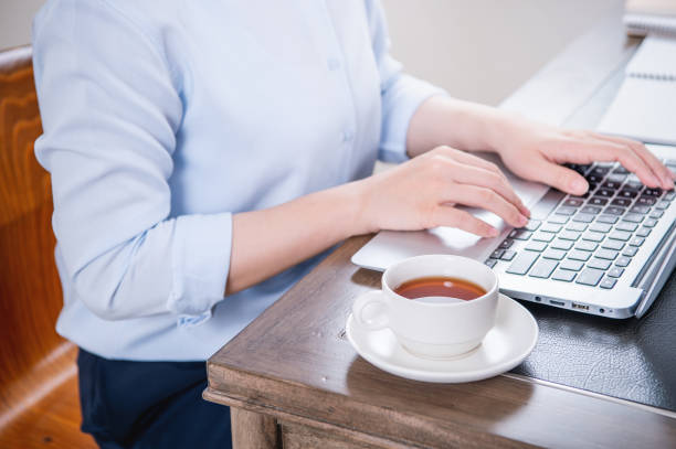 concept d’affaires. femme dans la chemise bleue tapant sur l’ordinateur avec le café sur la table de bureau, rétroéclairage, effet d’éblouissement de soleil, fermer, vue latérale, espace de copie - desk on the phone sitting table photos et images de collection