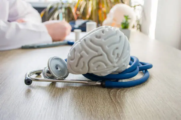 Photo of Concept photo of diagnosis and treatment of brain nervous. In foreground is model of brain near stethoscope on table in background blurred silhouette doctor at table, filling medical documentation