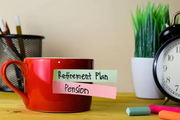 Photo of Retirement Plan and Pension. Handwriting on sticky notes in clothes pegs on wooden office desk