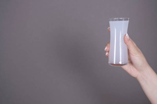 An adult woman is raising her hand to toast with traditional Turkish drink raki glass on gray background Only adult woman's arm is raising to toast with their raki glasses on pastel gray background serbian raki stock pictures, royalty-free photos & images