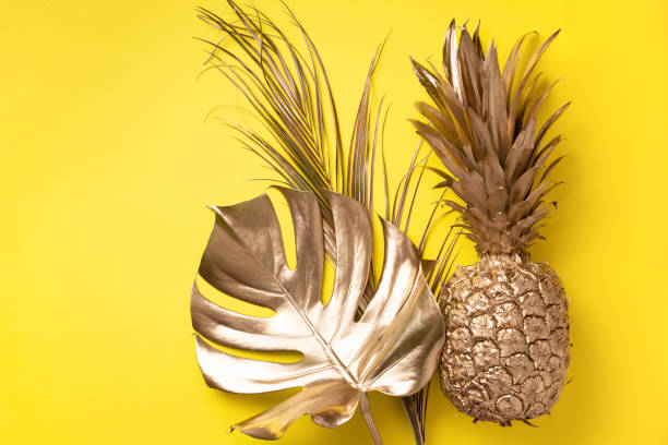 Creative layout. Gold pineapple and golden palm, monstera on yellow background with copy space. Top view. Tropical flat lay. Exotic food concept, crazy trend. Banner