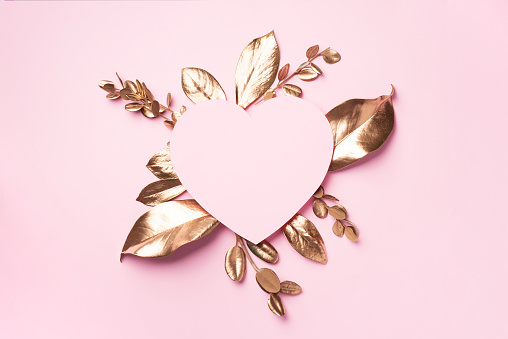 Golden leaves, heart shaped paper on pink background with copy space. Top view. Copy space. Summer and autumn concept. Creative design elements for invitation, wedding cards, valentines day, greeting cards