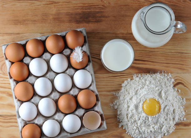 chicken eggs are raw in the tray. the shell is white and brown in eggs. next to the pitcher with milk and flour. the egg yolk is placed in the flour. - baking flour ingredient animal egg imagens e fotografias de stock