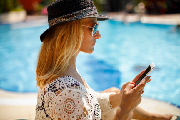istock Attractive woman texting by the swimming pool 1155450366