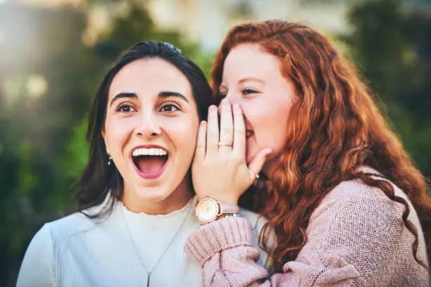 Shot of a woman whispering something into her friend's ear