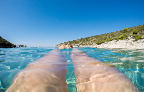 personal point of view of woman legs, swimming in beautiful blue adriatic sea at porat beach, in bisevo island, croatia - leg split imagens e fotografias de stock