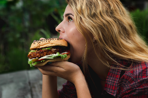 Student consume fast food. Girl bite of very big burger in the garden