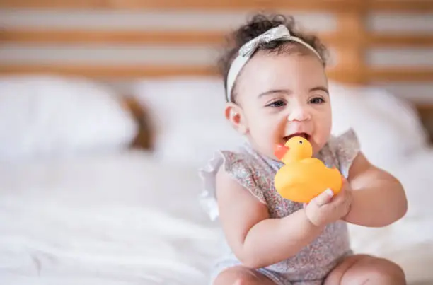 Shot of a cute baby girl sitting on bed enjoying playing with a rubber duck