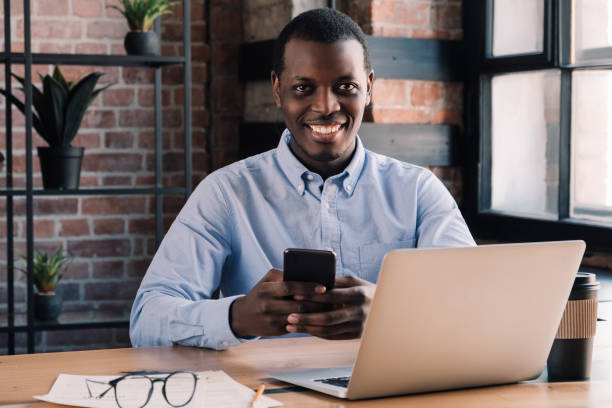 istock African man spending time in office with phone in hand, smiling at camera and feeling confident 1155458439