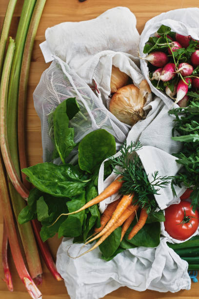 istock Zero waste grocery shopping concept,flat lay. Reusable eco friendly bags with fresh vegetables carrots,tomatoes, spinach,arugula, mushrooms,rhubarb,onions on wooden table. ban plastic. 1155459244