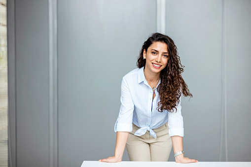 Portrait of beautiful young business woman in casuals standing by table in meeting room