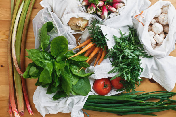 istock Zero waste grocery shopping concept,flat lay. Reusable eco friendly bags with fresh vegetables carrots,tomatoes, spinach,arugula, mushrooms,rhubarb,onions on wooden table. ban plastic. 1155461445