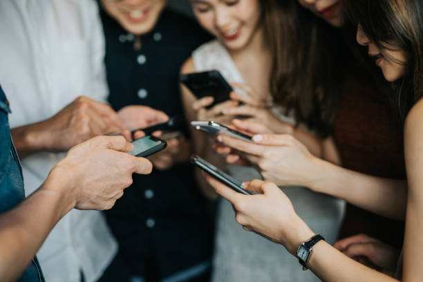 Circle of young Asian man and woman using smartphone during party stock photo