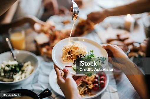 istock Group of joyful young Asian man and woman having fun, passing and sharing food across table during party 1155466574