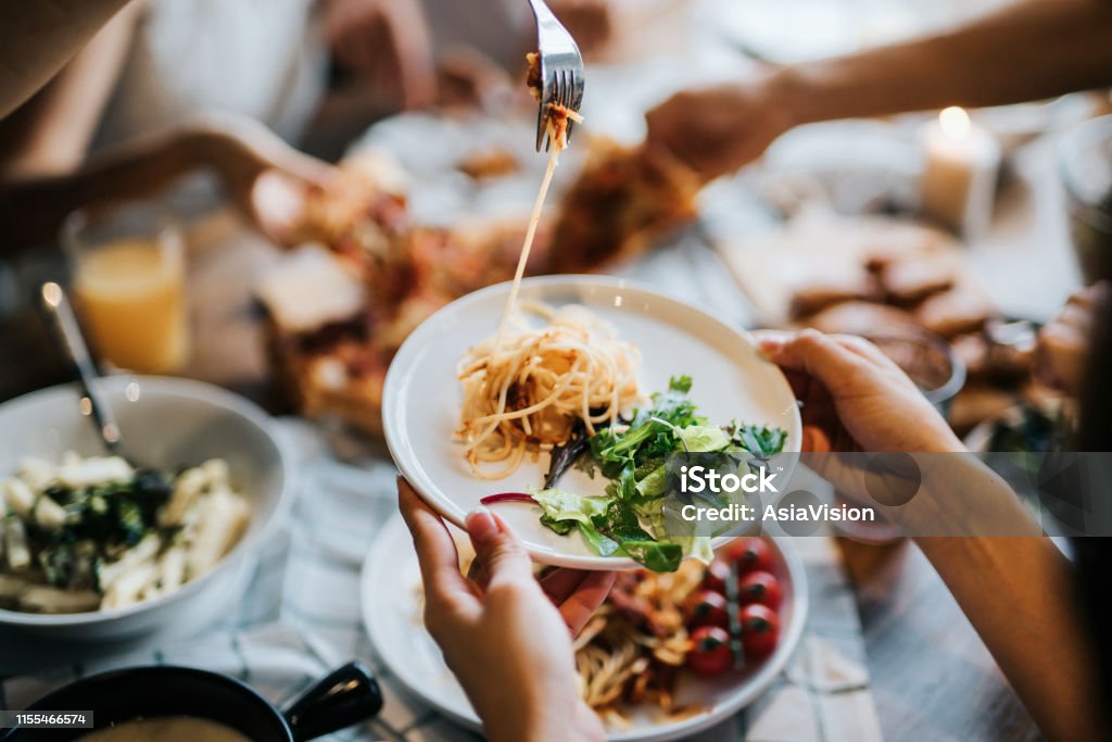 Group of joyful young Asian man and woman having fun, passing and sharing food across table during party Food Stock Photo