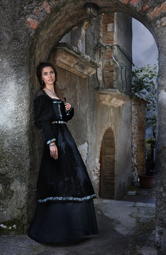 Young beautiful woman in a medieval dress standing in the inner courtyard of an old mansion