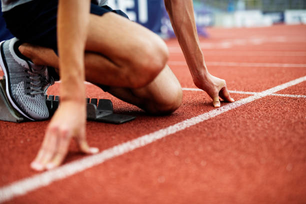 Unrecognizable Athlete Preparing For Start On Running Track. Unrecognizable Athlete Preparing For Start On Running Track. Young Muscular Male Athlete take a position on running track field. Low Section of Athlete on running track. track and field stock pictures, royalty-free photos & images