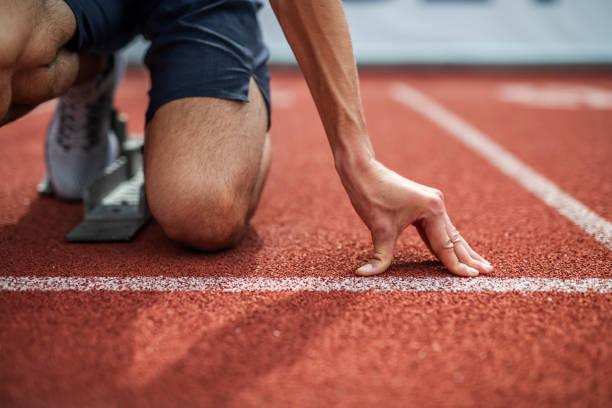 Unrecognizable Athlete Preparing For Start On Running Track. Unrecognizable Athlete Preparing For Start On Running Track. Young Muscular Male Athlete take a position on running track field. Low Section of Athlete on running track. track starting block stock pictures, royalty-free photos & images