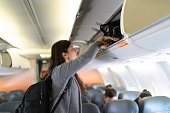 Woman putting luggage in overhead bin in airplane