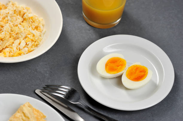 zwei hälften hartgekochtes ei auf einem weißen teller. im rahmen des tellerrandes mit rührei, besteck, einem glas mit saft. - fork plate isolated scrambled eggs stock-fotos und bilder