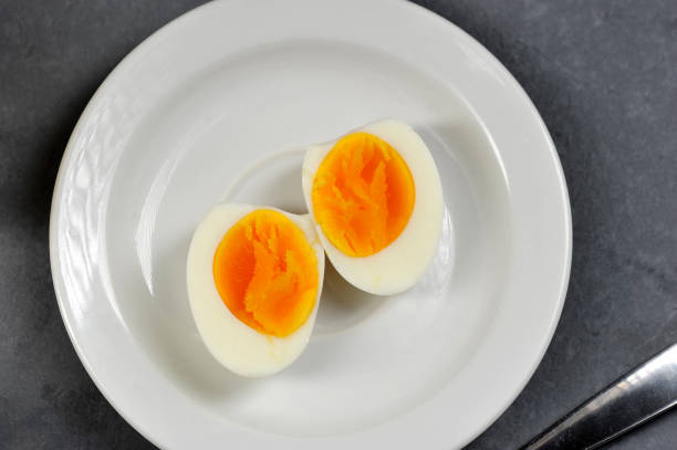 due metà di un uovo di gallina sodo. l'uovo giace su un piatto bianco. sfondo grigio. vista dall'alto. - hard cooked egg foto e immagini stock