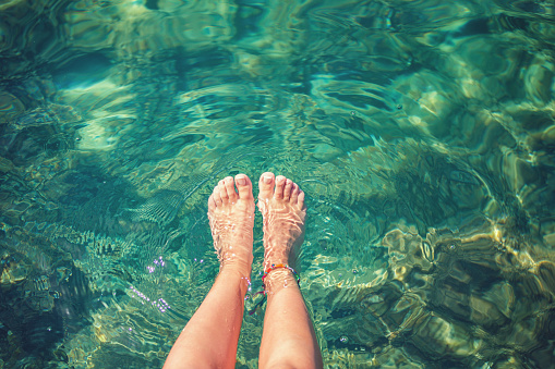 Teenage girl relaxing by the sea, she diving feet in emerald green water on the Greek island