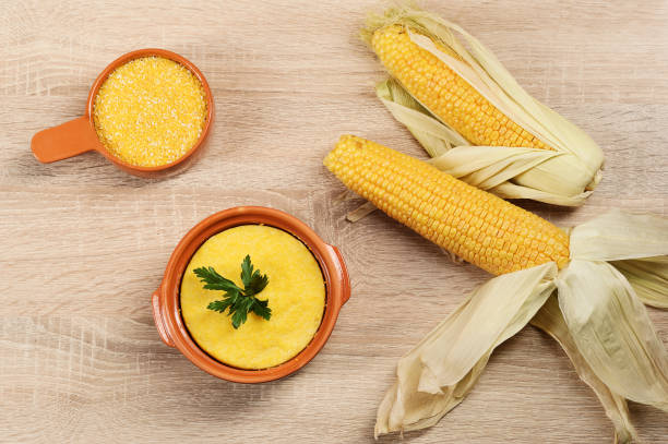 Corn hominy porridge in a clay pot. Corn flour in a clay bowl and cob of ripe corn.