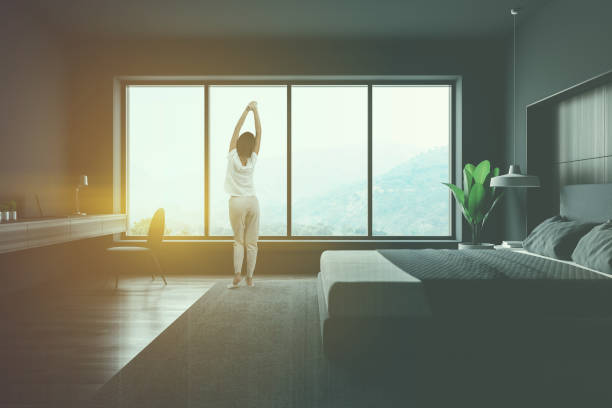 istock Woman looking in gray bedroom window 1155509747