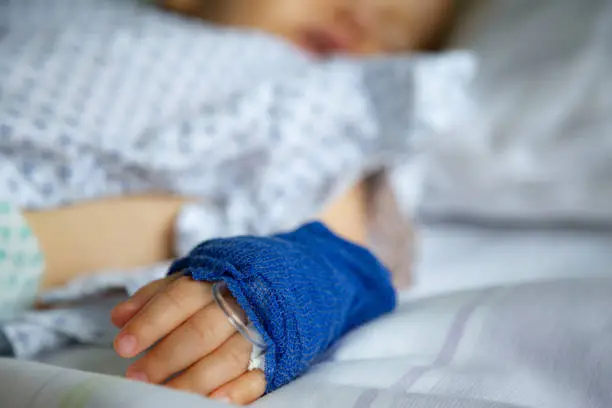 Photo of Sleeping sick child with peripheral venous line on his left hand in hospital