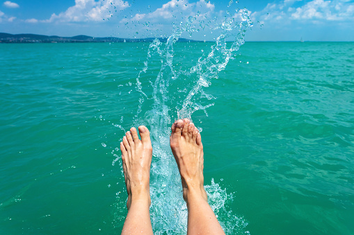 A happy girl woman is kicking feet on a sea lake and splashing water on a sail boat summertime holiday